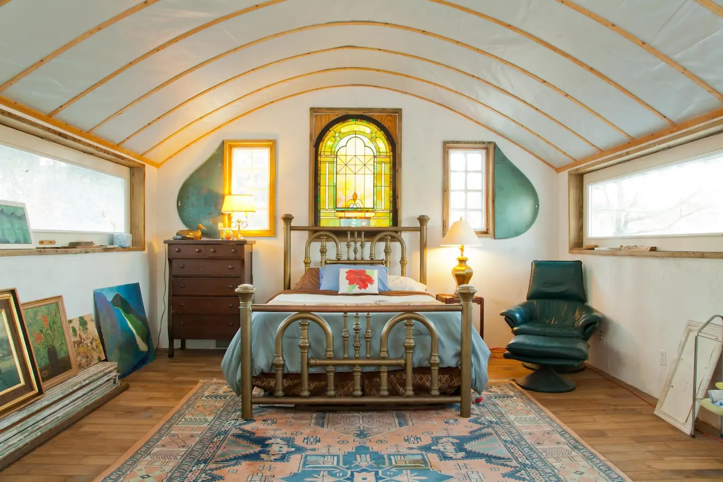 A brass bed beneath a stained-glass window in the curved-ceiling loft