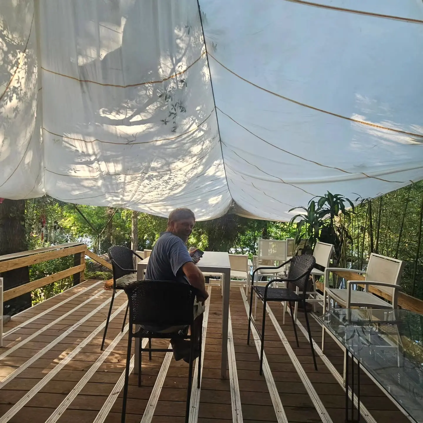 A white sail stretched over the riverside deck, chairs set out in the shade