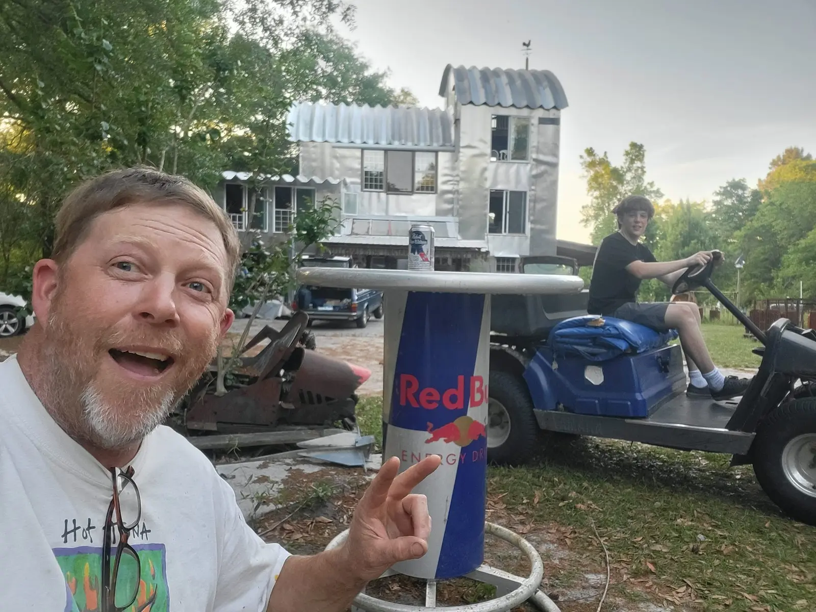 Allen Walker grinning in front of the Garagemahal workshop while a guest rides past on a golf cart