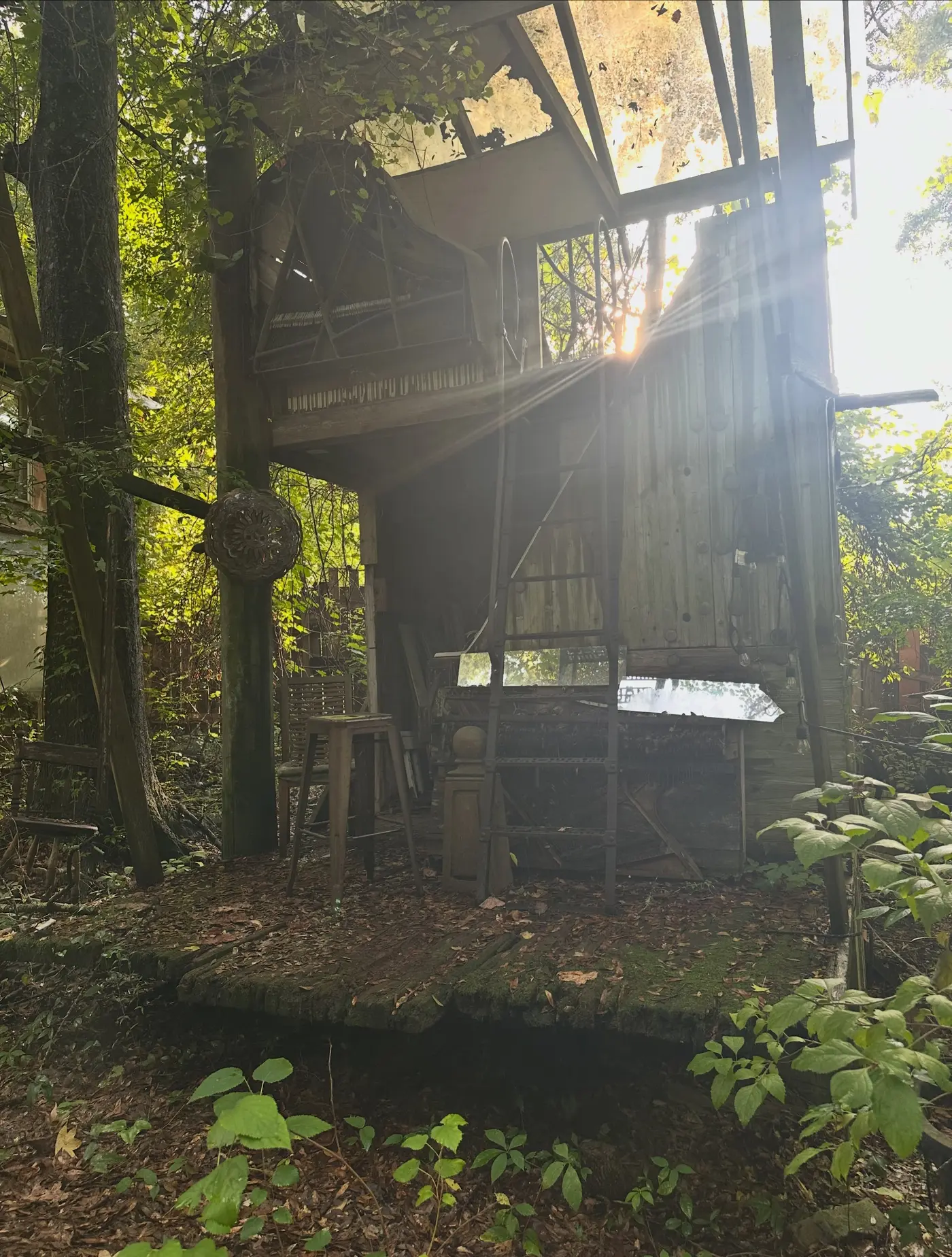 The three-storey piano playhouse in the woods, an upright piano built into its upper floor, sun flaring through the trees