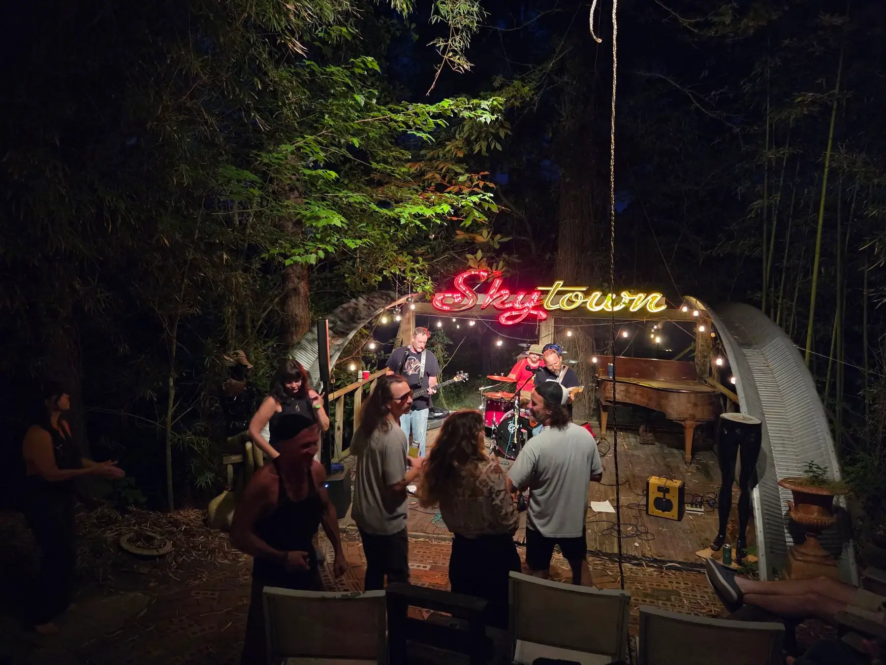 The Skytown stage glowing in neon at night with a crowd gathered in the pines